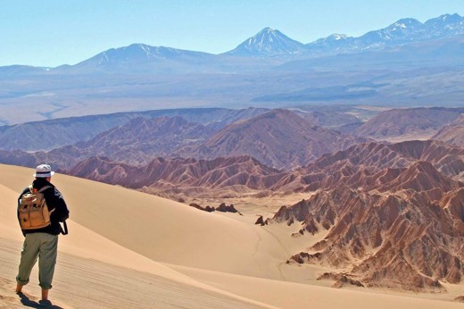 Hiker explores the vast, sunlit dunes of Chile's Atacama Desert with Andes backdrop. 