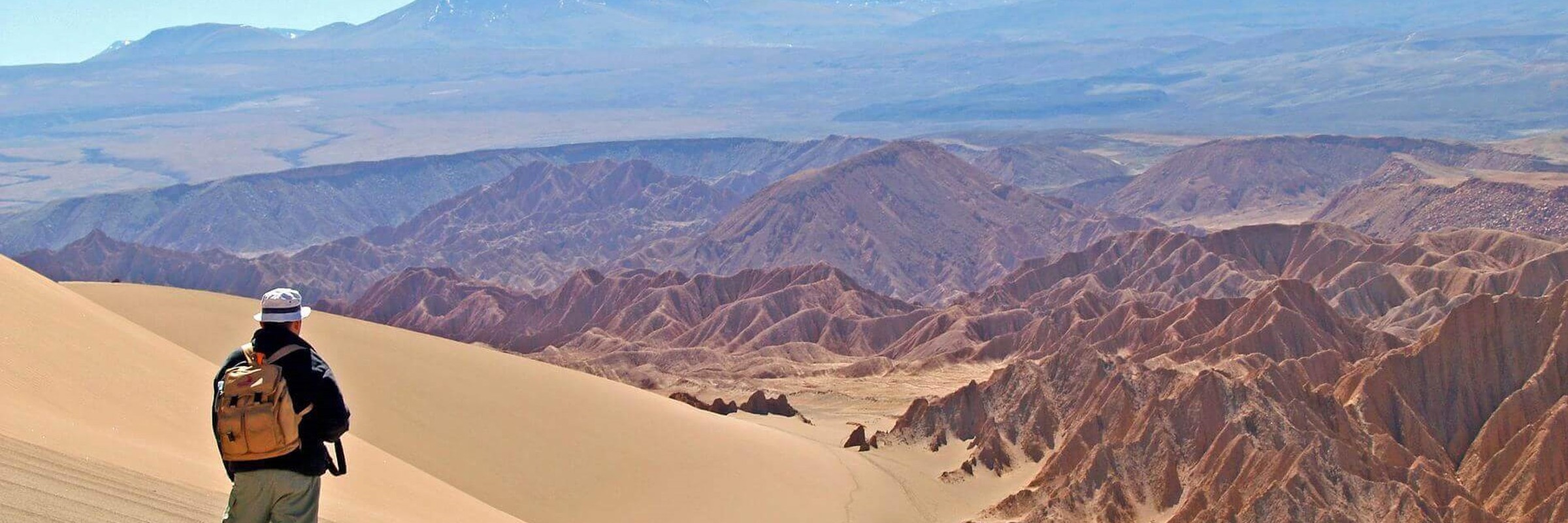 Hiker explores the vast, sunlit dunes of Chile's Atacama Desert with Andes backdrop. 