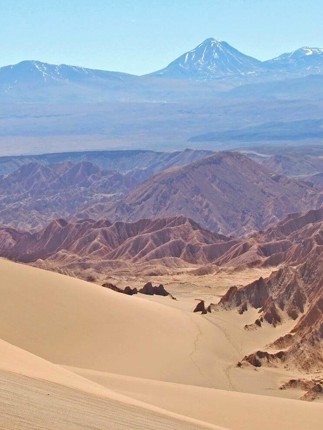 Hiker explores the vast, sunlit dunes of Chile's Atacama Desert with Andes backdrop.