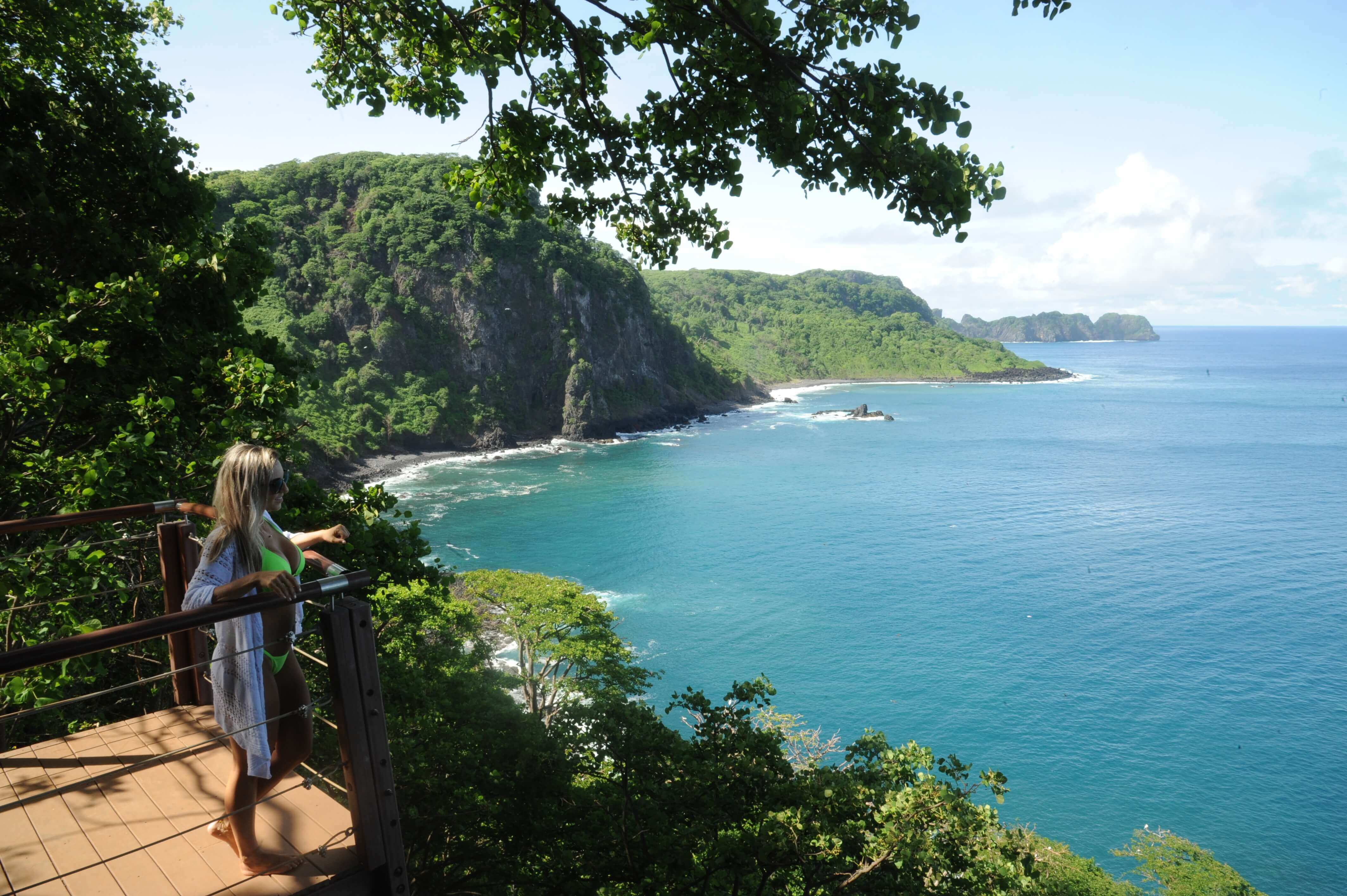 Woman at a cliffside viewpoint overlooking the rugged coastline and turquoise waters of Fernando de Noronha. 
