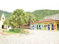 Charming village square with colourful shops and a small church in Ilha Grande, surrounded by lush green hills. 