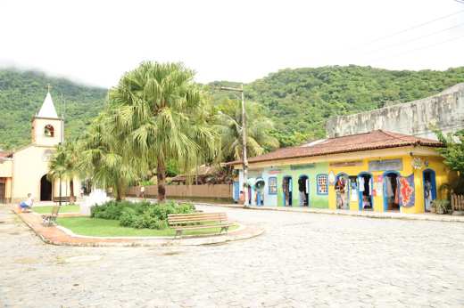 Charming village square with colourful shops and a small church in Ilha Grande, surrounded by lush green hills. 