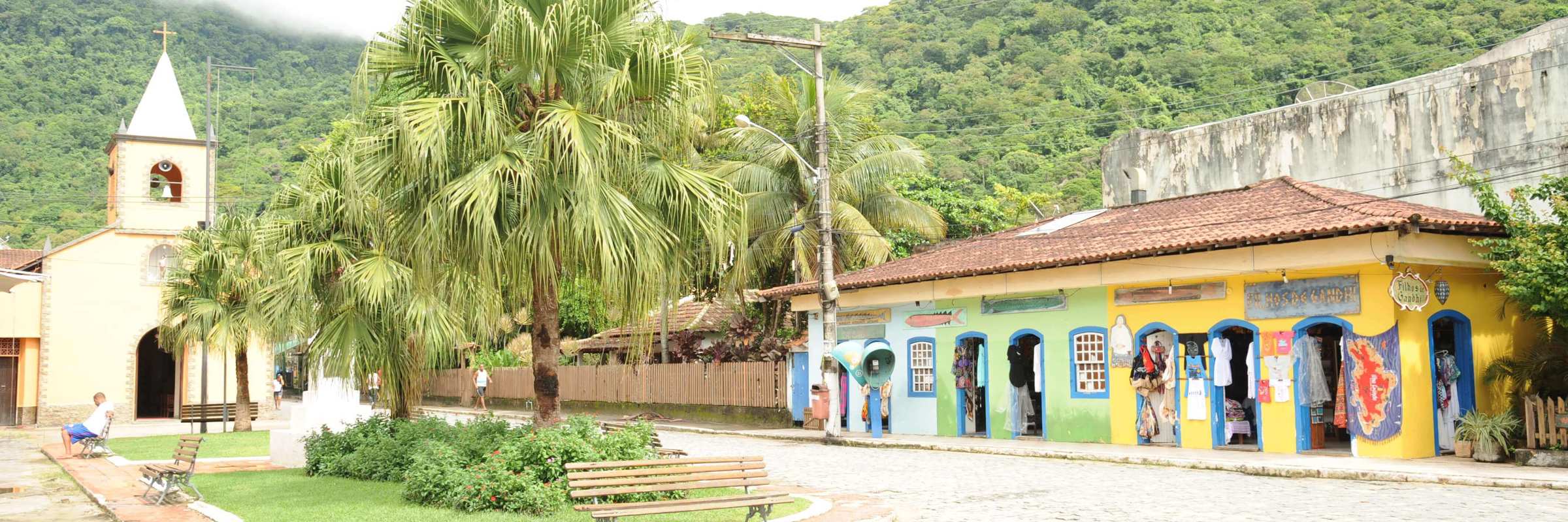 Charming village square with colourful shops and a small church in Ilha Grande, surrounded by lush green hills. 