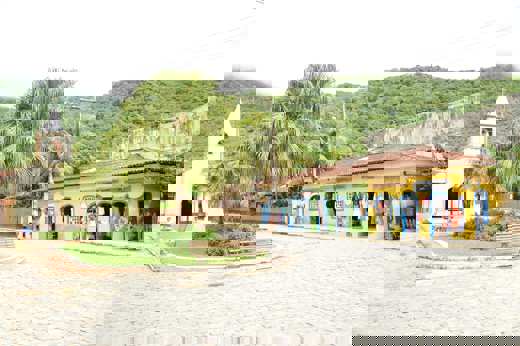 Charming village square with colourful shops and a small church in Ilha Grande, surrounded by lush green hills. 