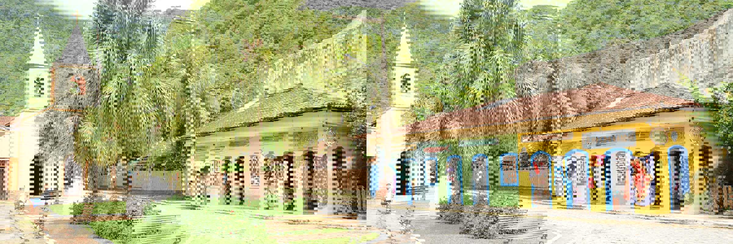 Charming village square with colourful shops and a small church in Ilha Grande, surrounded by lush green hills. 