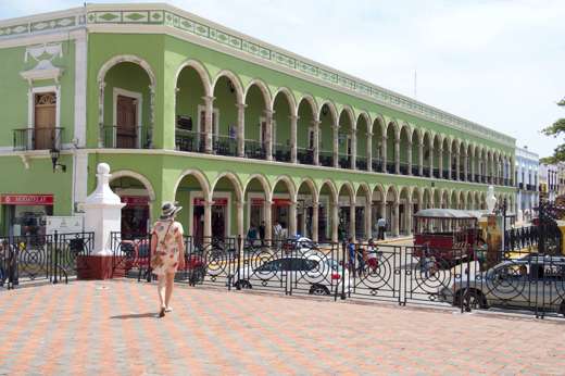 Historic green arcade building on Merida's Plaza Grande, Yucatan, with colonial arches, statue, and pedestrian view. 