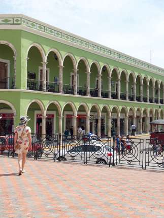Historic green arcade building on Merida's Plaza Grande, Yucatan, with colonial arches, statue, and pedestrian view. 