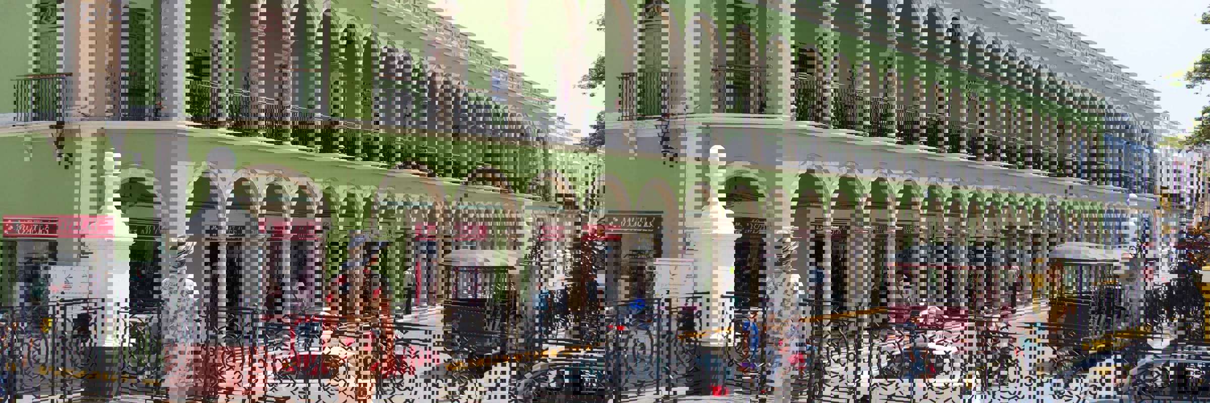 Historic green arcade building on Merida's Plaza Grande, Yucatan, with colonial arches, statue, and pedestrian view. 