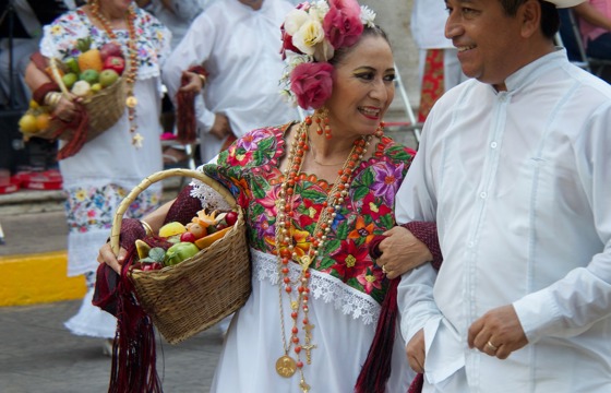 Couple in traditional Yucatan folk costumes dancing during a colourful festival in Mexico, with musicians in the background.