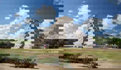 The Temple of Kukulcan at Chichen Itza rises under a bright sky, showcasing ancient Mayan architectural brilliance. 