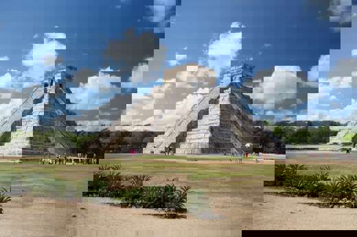 The Temple of Kukulcan at Chichen Itza rises under a bright sky, showcasing ancient Mayan architectural brilliance. 