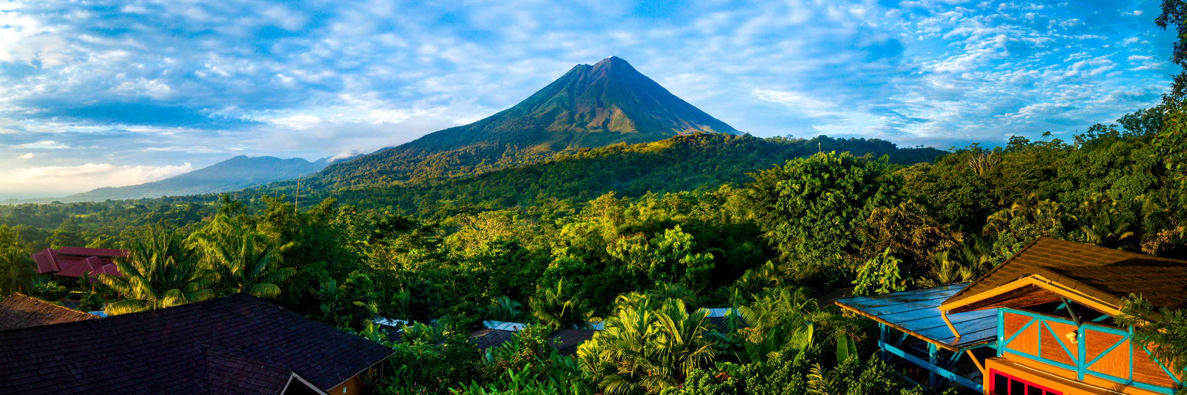 Arenal Volcano rises above the tropical forest of Costa Rica, framed by colorful lodges. 