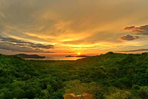 Golden sunset over the forested hills of Guanacaste, with the sun setting above the Pacific horizon. 