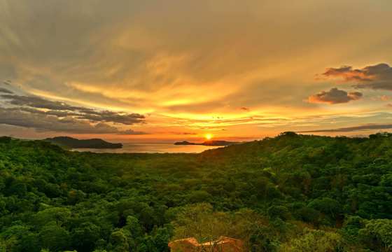 Golden sunset over the forested hills of Guanacaste, with the sun setting above the Pacific horizon. 