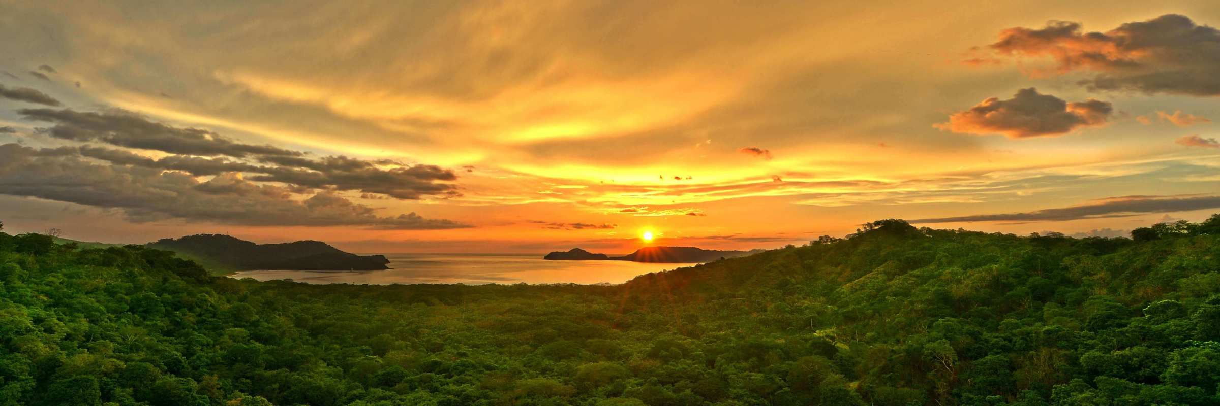 Golden sunset over the forested hills of Guanacaste, with the sun setting above the Pacific horizon. 