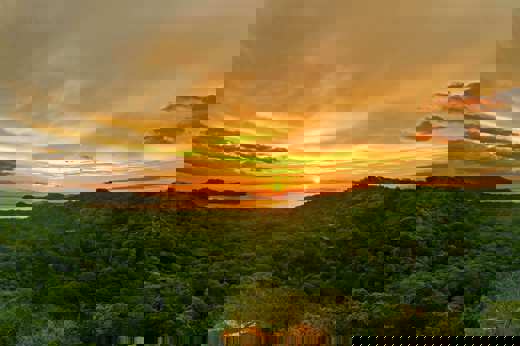Golden sunset over the forested hills of Guanacaste, with the sun setting above the Pacific horizon. 