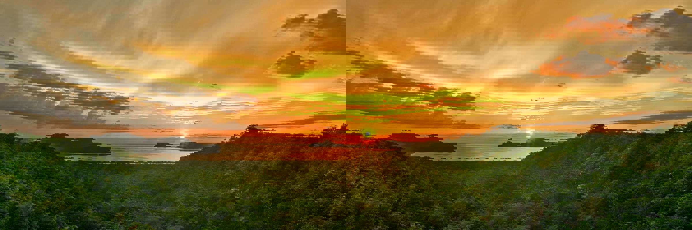 Golden sunset over the forested hills of Guanacaste, with the sun setting above the Pacific horizon. 