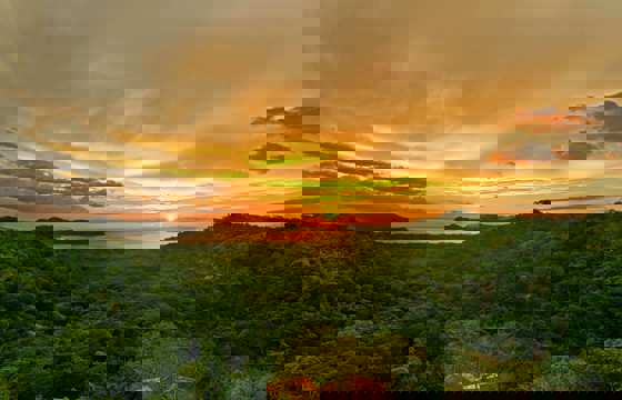Golden sunset over the forested hills of Guanacaste, with the sun setting above the Pacific horizon.