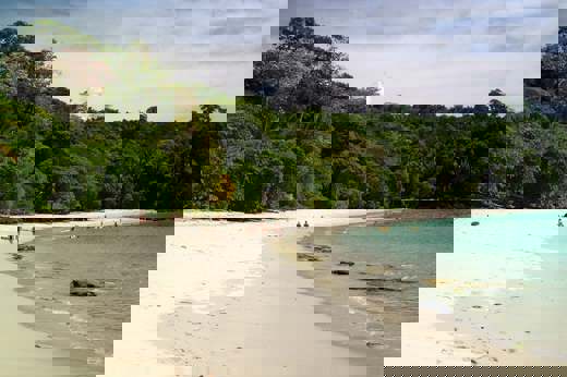 White sandy beach backed by lush rainforest in Manuel Antonio National Park, with people walking along the the shore and calm turquoise waters. 