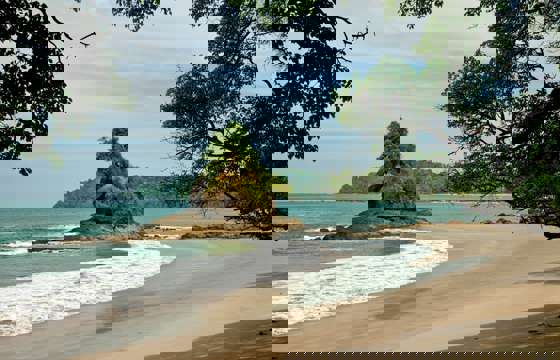 A rocky islet rises just offshore as gentle waves lap the peaceful sands of Manuel Antonio.