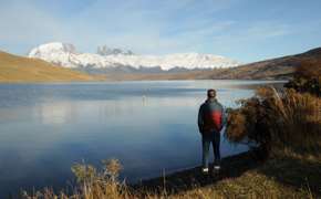Traveler admires the reflection of the Paine Massif in a still Patagonia lake under clear skies in Torres del Paine, Chile. 