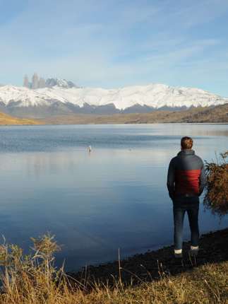 Traveler admires the reflection of the Paine Massif in a still Patagonia lake under clear skies in Torres del Paine, Chile. 