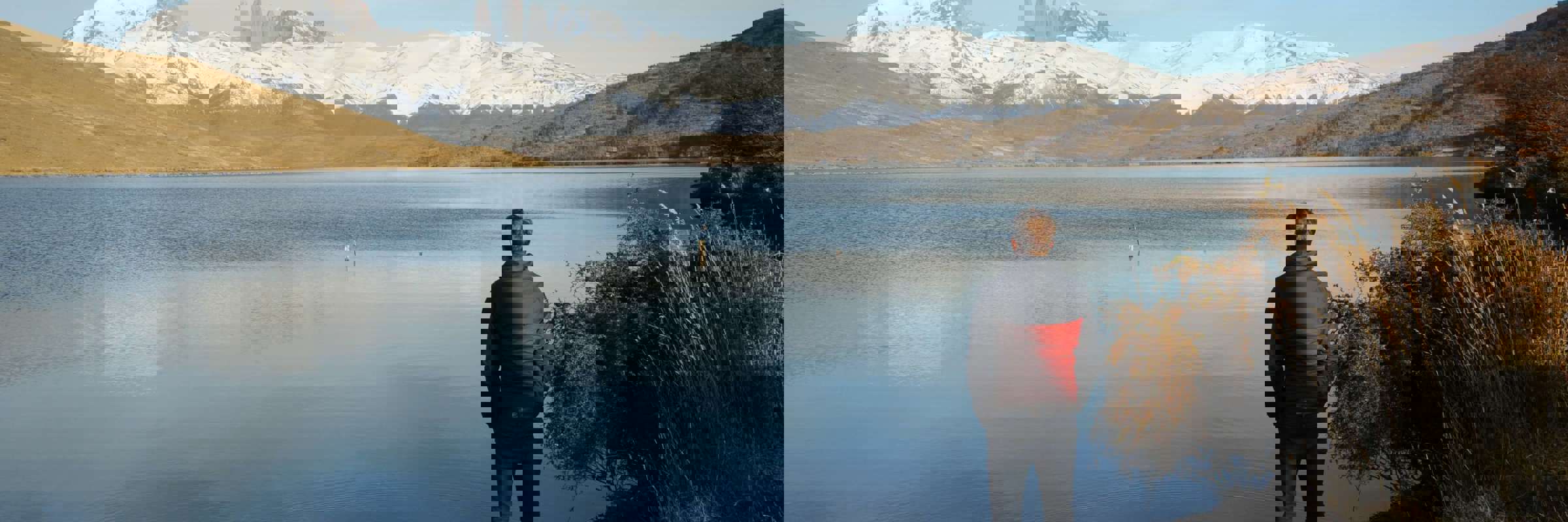 Traveler admires the reflection of the Paine Massif in a still Patagonia lake under clear skies in Torres del Paine, Chile. 