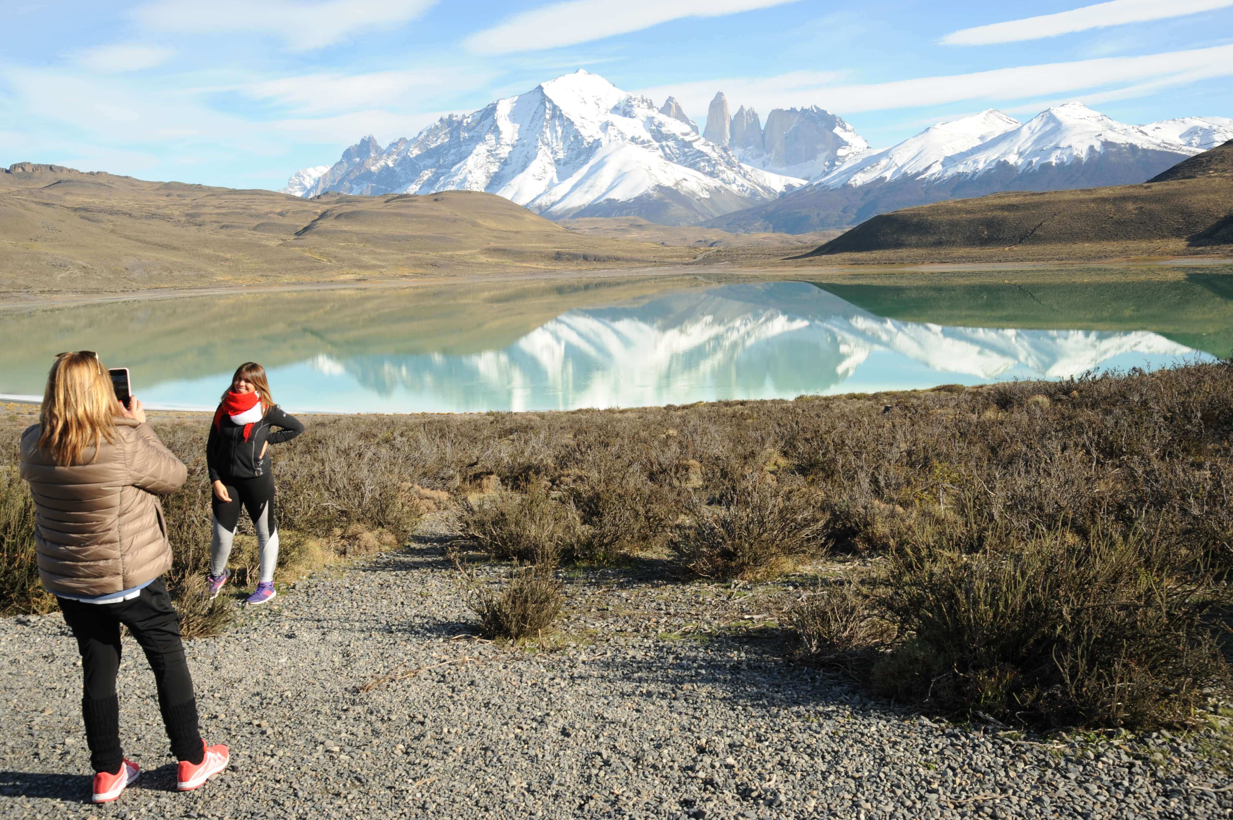 Travelers photograph the stunning mirrored reflection of Torres del Paine's peaks on a still Patagonia lake. 