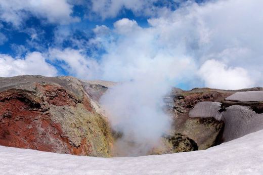 View of the steaming crater of Villarrica Volcano near Pucon, Chile, surrounded by snow and dramatic skies. 