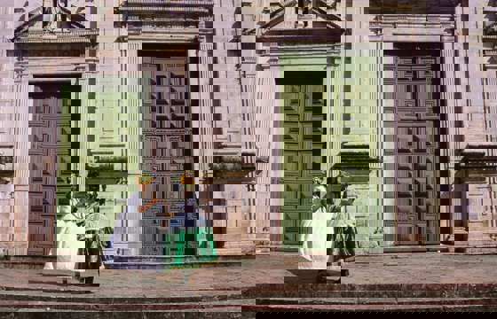 Women in traditional Baiana dresses standing outside historic green doors in Salvador's Pelourinho district, Bahia, Brazil.