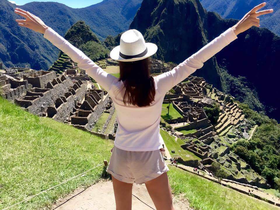 Woman with arms raised overlooking Machu Picchu and the Andes Mountains Peru. 