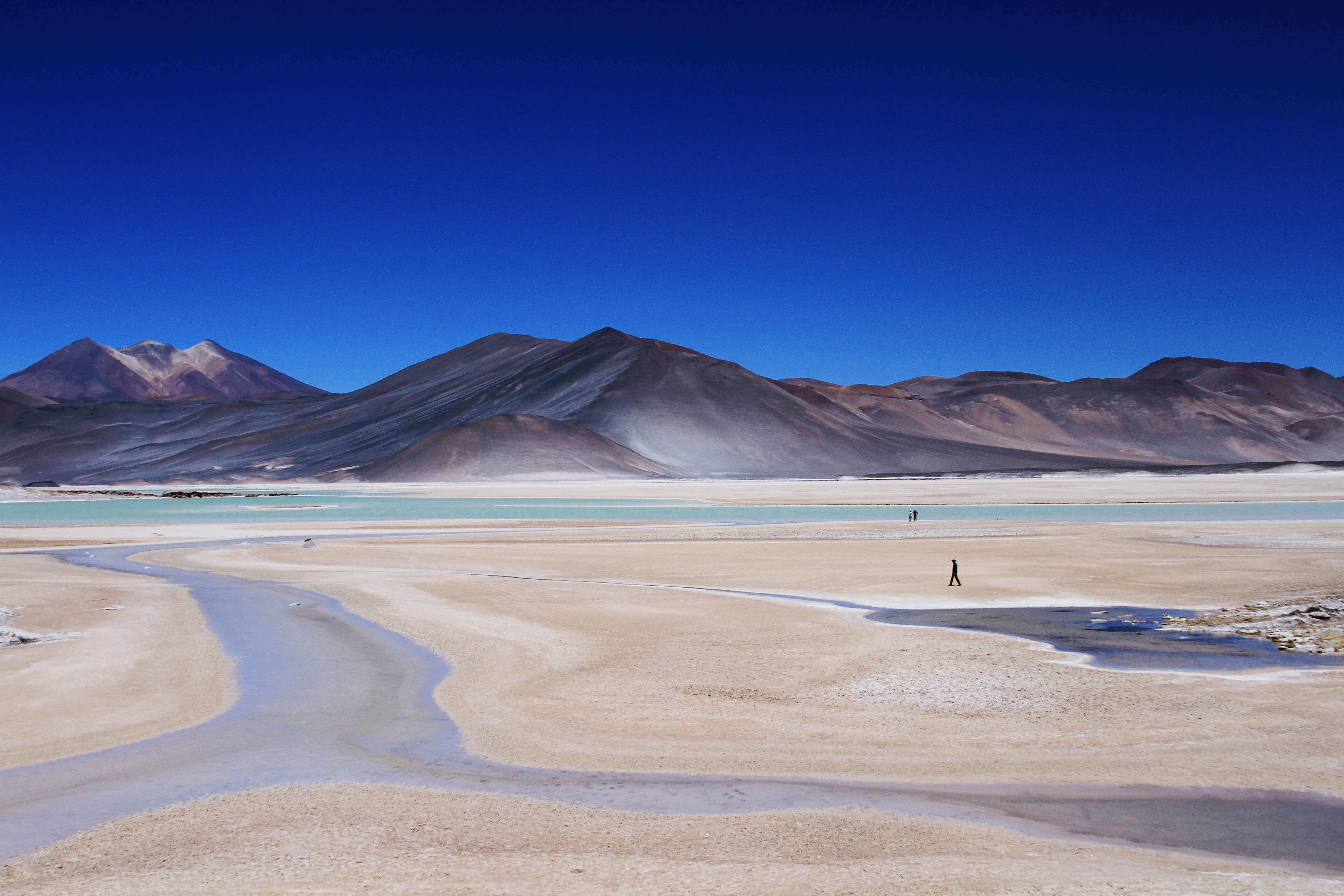 Vast salt flats with volcanoes in the distance under a deep blue sky in the Atacama Desert. 