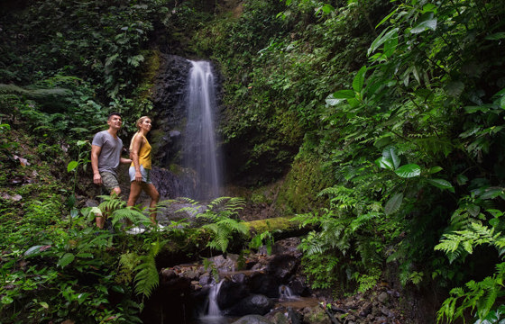 Couple hiking through lush rainforest to a hidden waterfall in Costa Rica's Tenorio National Park.