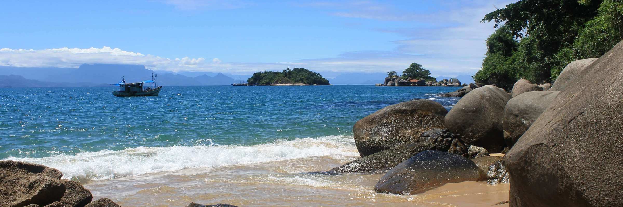 Small boat anchored off a secluded beach with rocky shoreline on Ilha Grande. 