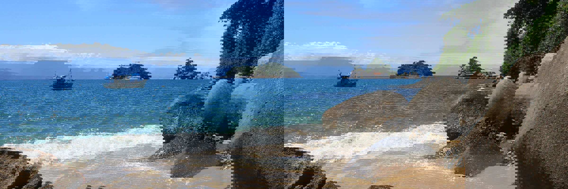 Small boat anchored off a secluded beach with rocky shoreline on Ilha Grande. 