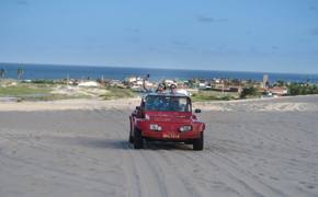 Red beach buggy driving  across sand dunes in Jericoacoara with ocean and coastal town in the background. 
