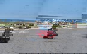 Red beach buggy driving  across sand dunes in Jericoacoara with ocean and coastal town in the background. 