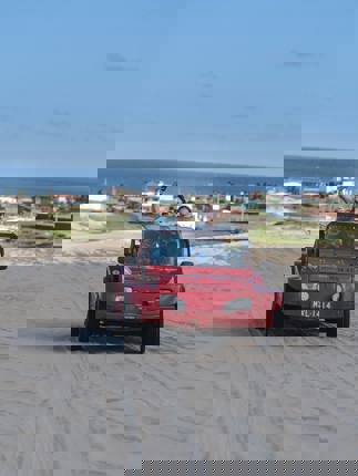 Red beach buggy driving  across sand dunes in Jericoacoara with ocean and coastal town in the background. 