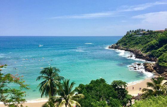 Scenic view of Puerto Escondido's Pacific coastline in Mexico with turquoise waters, sandy beaches, and lush greenery. 