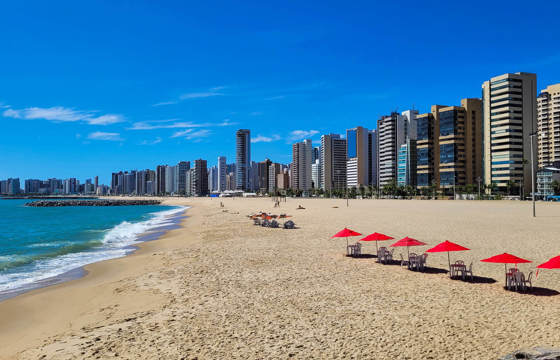 Wide sandy beach in Fortaleza with red umbrellas and a modern skyline along the northeastern coast of Brazil.